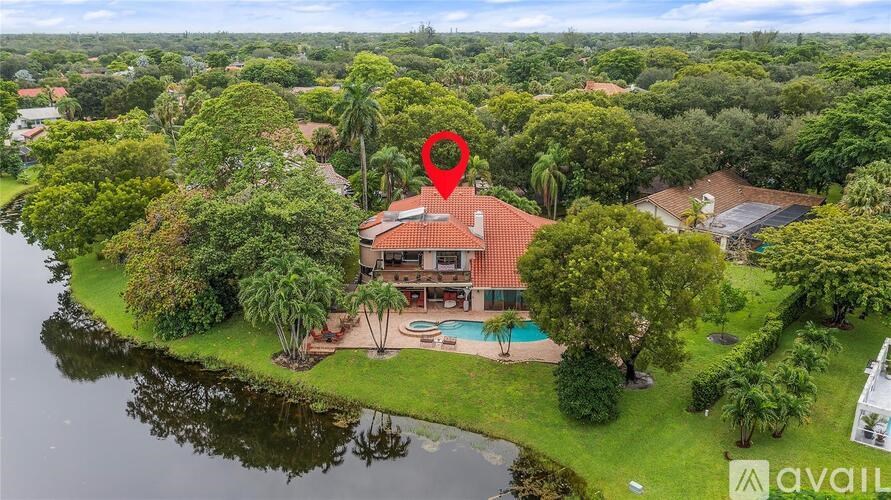 A house with a red roof is surrounded by greenery and has a pool in the backyard.