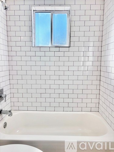 A white tiled bathroom with a window and a bathtub.