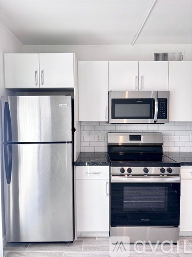 A kitchen with a stainless steel refrigerator, black countertops, and white cabinets.
