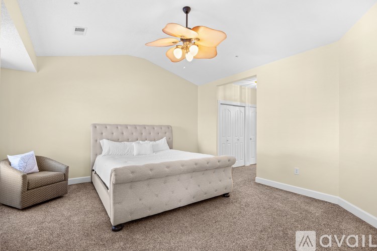 A bedroom with a bed, chair, and ceiling fan.