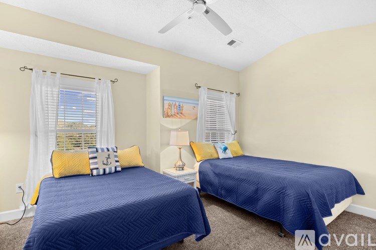 Two beds with blue bedspreads in a room with a ceiling fan.