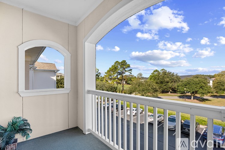 A balcony with a white railing and a view of a parking lot and trees.