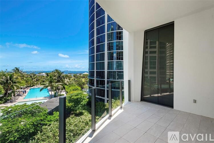 A balcony with a glass door overlooks a pool and palm trees.