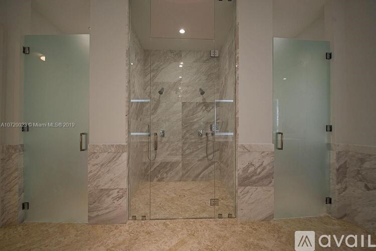 A bathroom with marble walls and a glass shower stall.