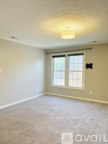 A room with a carpeted floor and a window with a view of a fence.