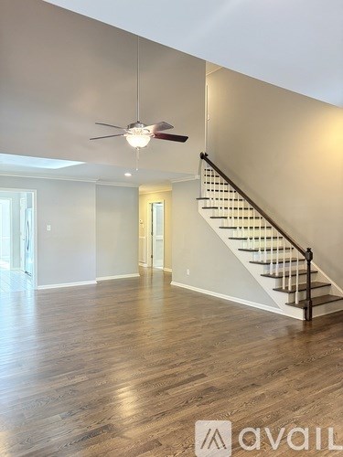 A spacious room with wooden floors and a staircase leading to the upper level.