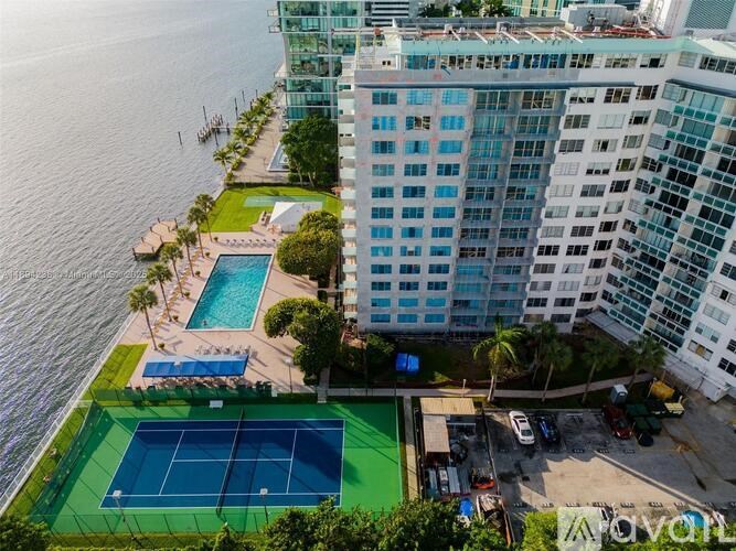 A tennis court is located on a rooftop next to a pool and a tall building.