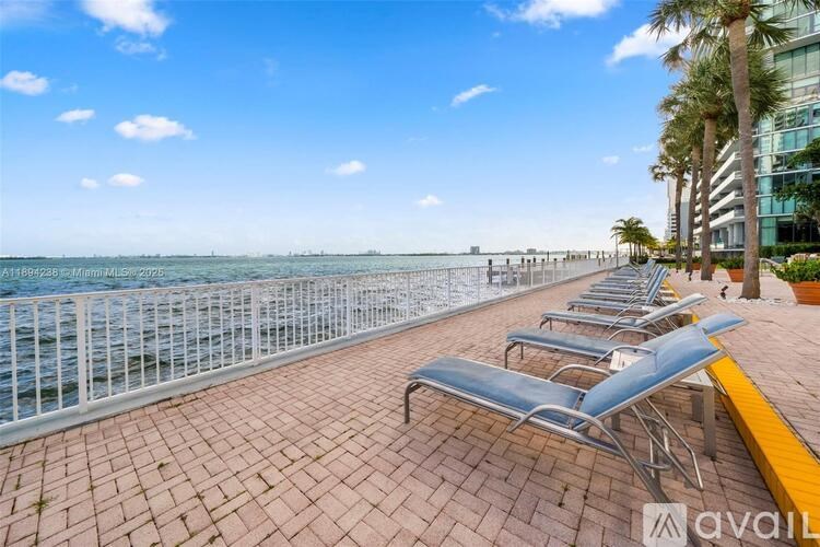A row of lounge chairs are set up on a patio overlooking the water.