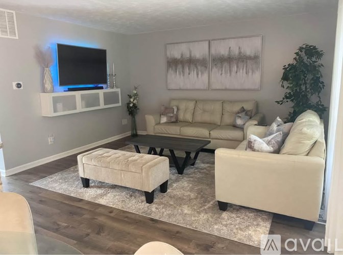 A living room with a beige couch, a white ottoman, and a TV mounted on the wall.