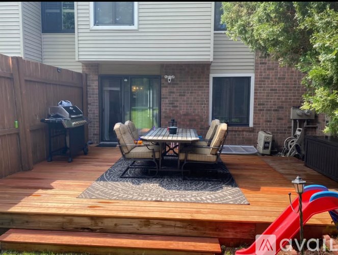 A wooden deck with a table and chairs is in front of a house.