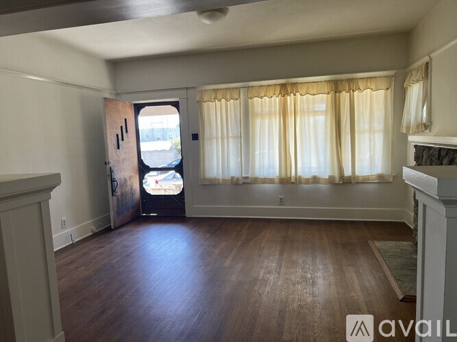 A room with wooden floors and a window with curtains.