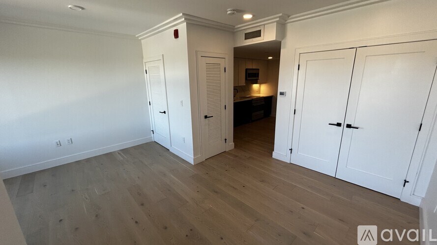 A room with white walls and wooden flooring, featuring a white cabinet with a door and a small shelf.