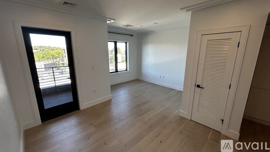 A room with wooden flooring and a large window with a view of a parking lot.