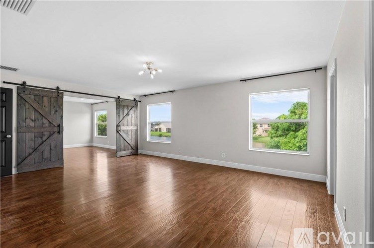 A spacious room with wooden floors and a large window showing a green landscape.
