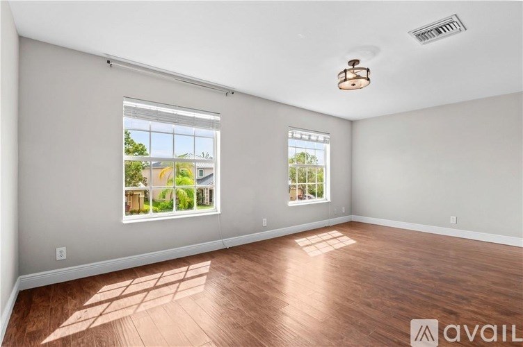 A room with wooden flooring and two windows showing an outdoor view.