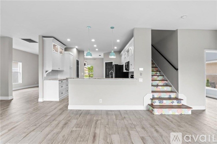 A modern kitchen with a white island and stairs with colorful tiles.