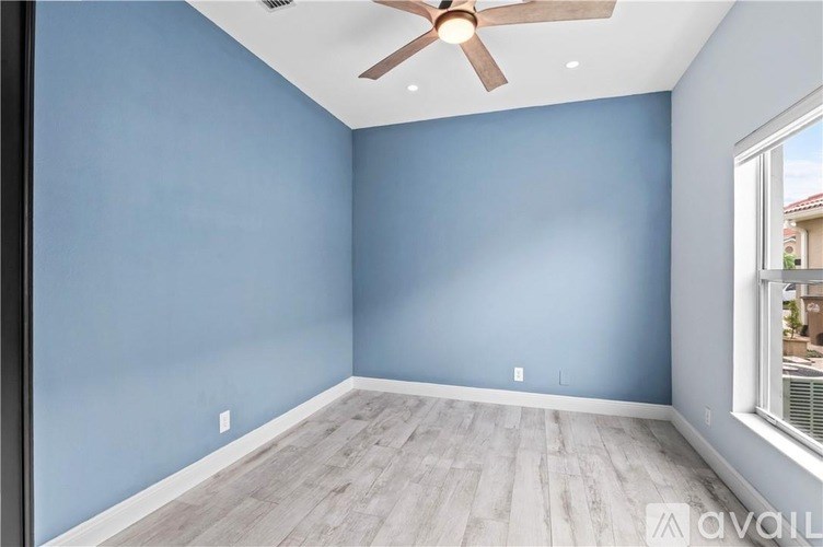 A room with a ceiling fan and light fixture, and a window with a view of a house.