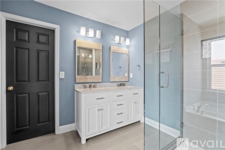 A bathroom with a black door, a white cabinet, and a glass shower door.