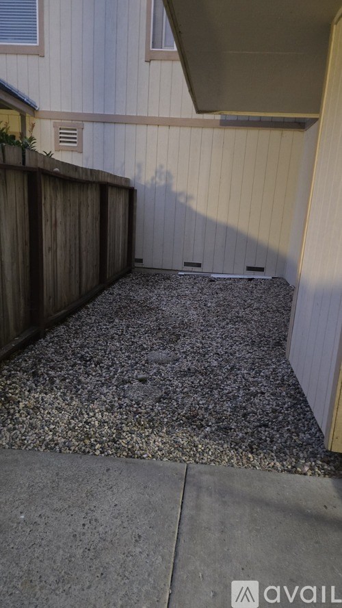 A gravel area in front of a wooden fence and house.
