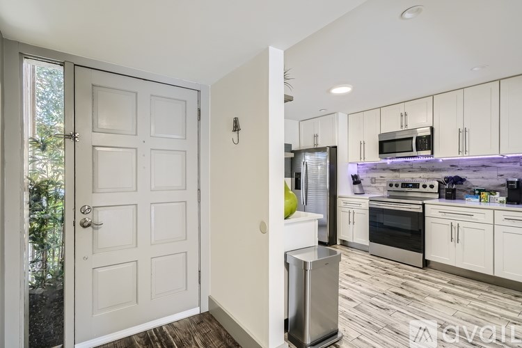 A white door is open to a kitchen with white cabinets and a microwave above the stove.