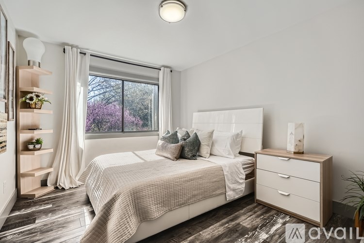 A bedroom with a large bed, a nightstand, and a window with a view of trees.