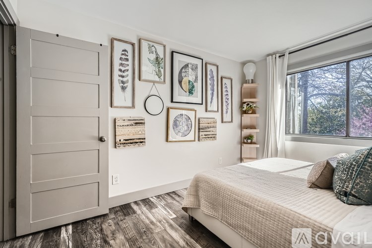 A bedroom with a bed, a wooden floor, a white door, and framed pictures on the wall.