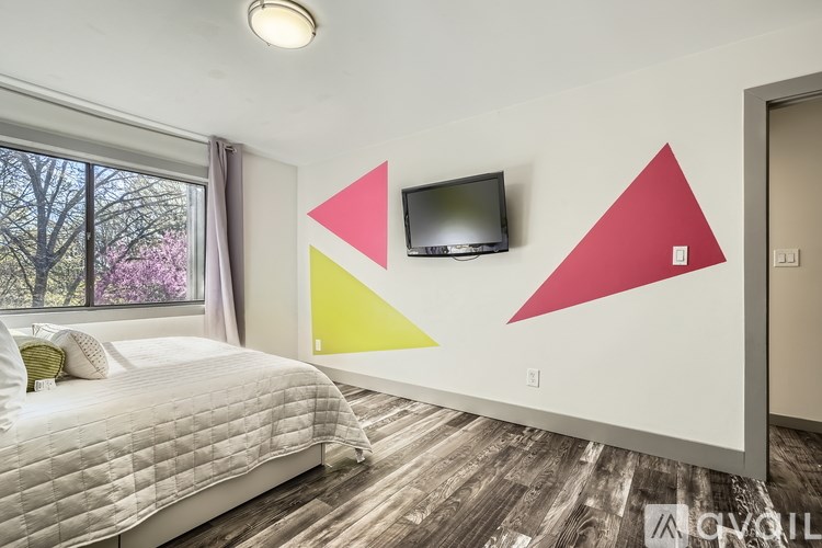 A bedroom with a bed, a window, and a TV mounted on the wall.