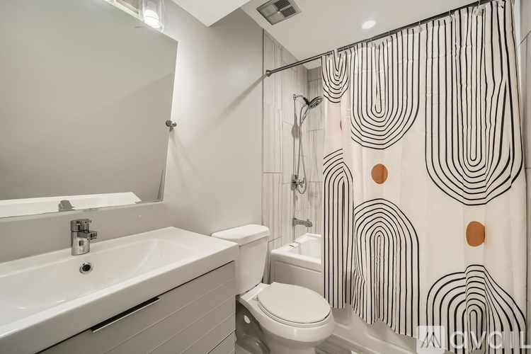 A white bathroom with a white sink, toilet, and a shower curtain with black and white stripes and circles.