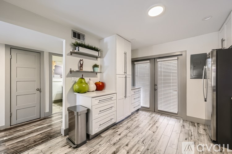 A kitchen with a black fridge, white cabinets, and a wooden floor.
