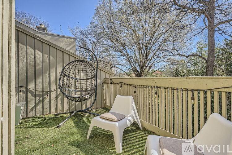 A white chair is on a wooden deck with a hanging chair and a tree in the background.