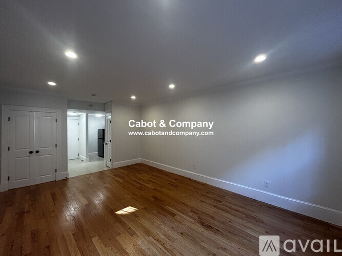 A room with wooden flooring and white walls, with a door on the left and a mirror on the right.