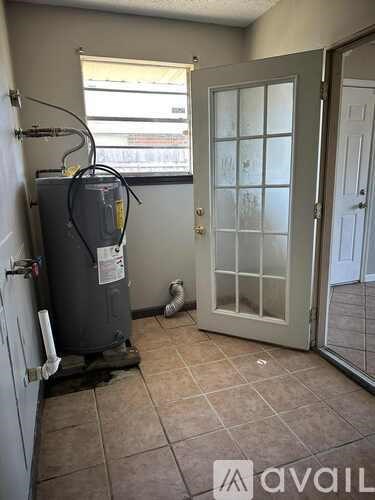 A room with a tiled floor, a window, a door, and a water heater.