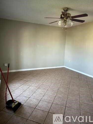 A room with a ceiling fan and a broom standing on the floor.