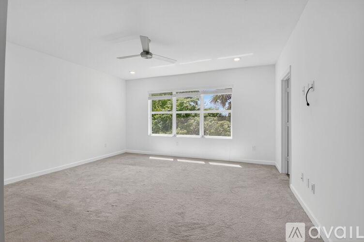 A spacious room with a ceiling fan and a large window with a view of trees outside.