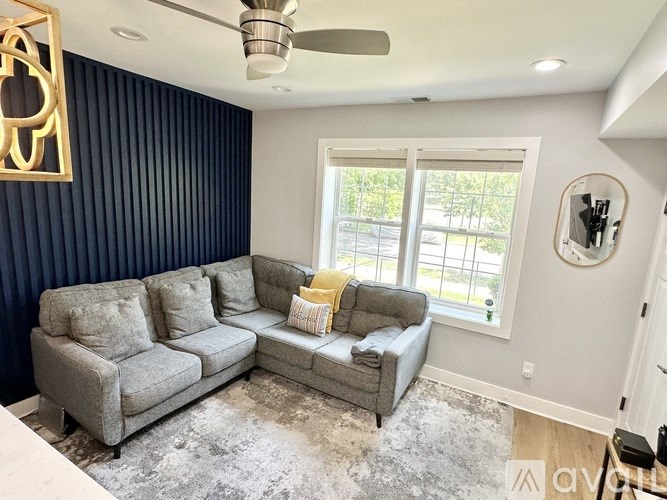 A grey couch with a yellow throw pillow sits in a room with a ceiling fan.