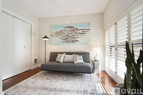 A living room with a grey couch and a large painting on the wall.