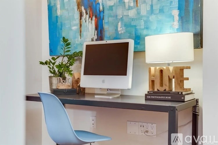 A blue chair sits in front of a desk with a computer monitor, a lamp, and a plant.