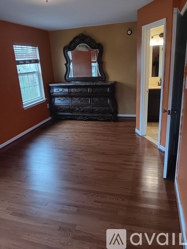 A room with a wooden floor and a large mirror above a dresser.