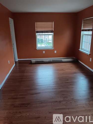 A room with wooden floors and two windows with blinds.
