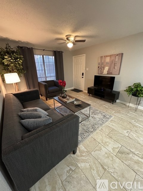 A living room with a grey couch, a black chair, a red rose, a television, and a painting on the wall.