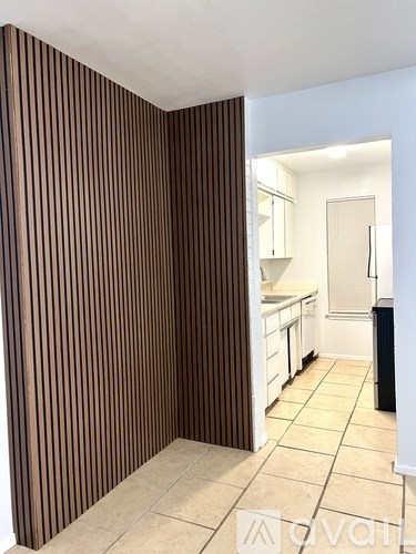 A room with a striped brown wall and a kitchen in the background.