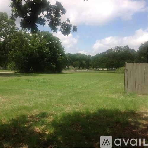 A grassy field with trees and a fence in the distance.