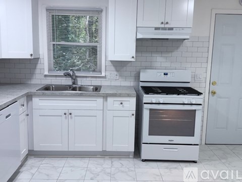 A white kitchen with a sink, stove, and cabinets.
