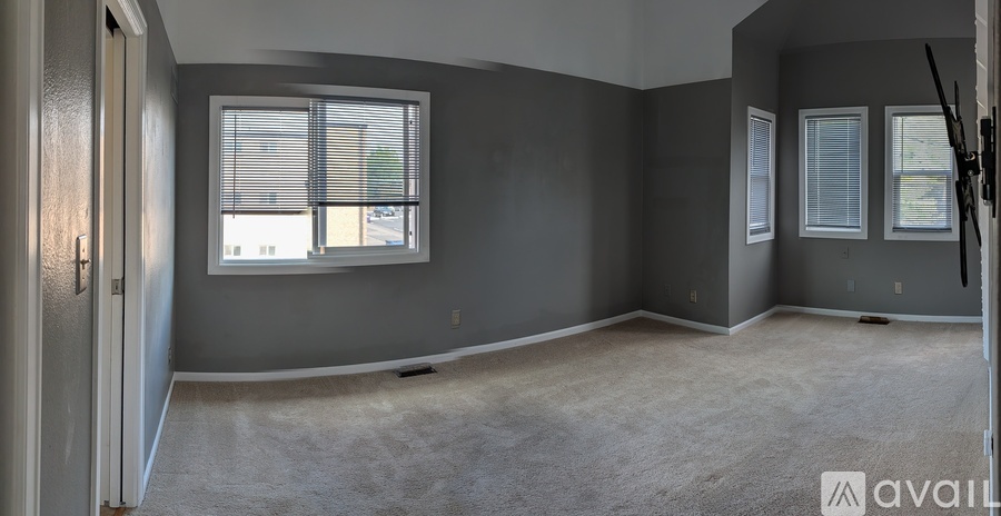 A room with grey walls and carpeted floor, featuring a large window with blinds and a door.