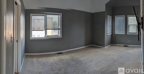A room with grey walls and carpeted floor, featuring a large window with blinds and a door.