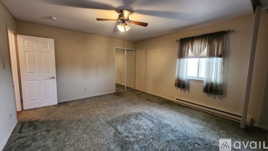 A room with a carpeted floor, a ceiling fan, and a window with curtains.