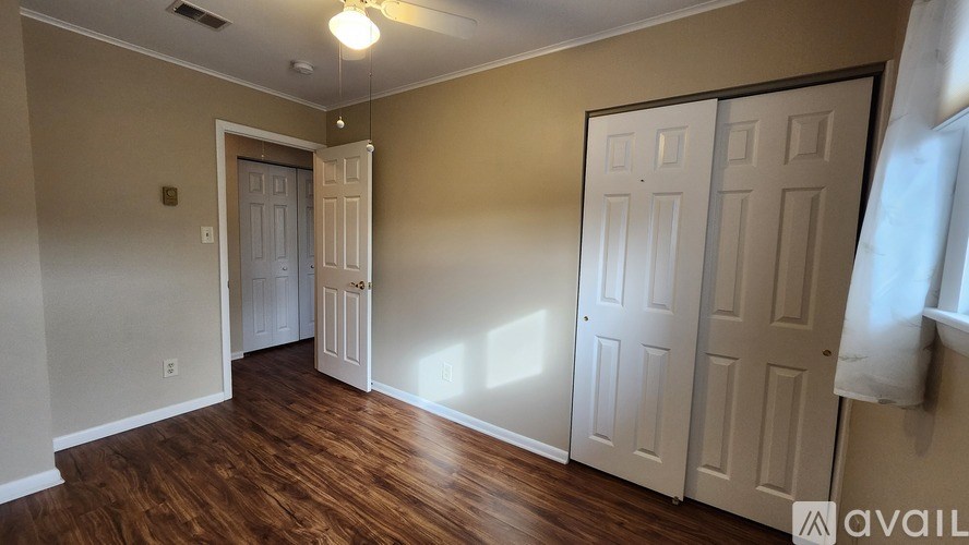 A room with wooden floors and white walls, with a door on the left and two closets on the right.