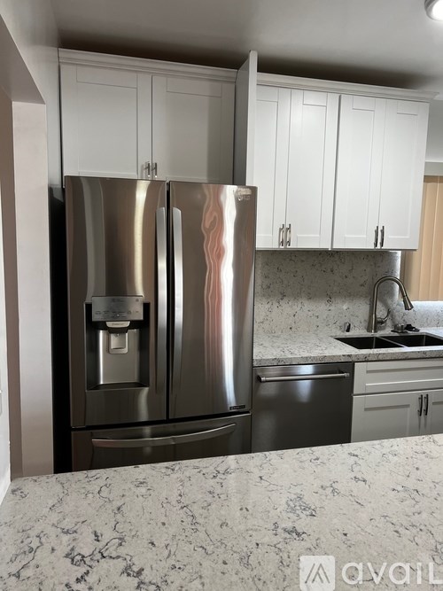 A kitchen with a stainless steel refrigerator and white cabinets.
