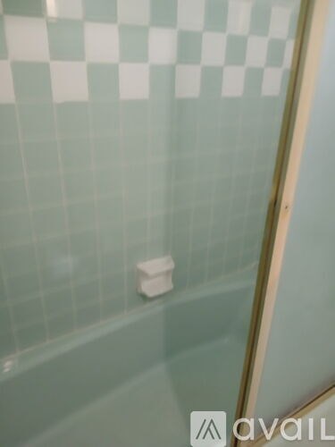 A white soap dish sits on a green tiled wall.