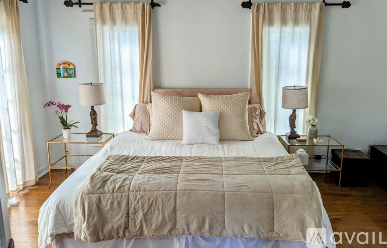A bed with a beige comforter and pillows is in the center of a room with two lamps on side tables.